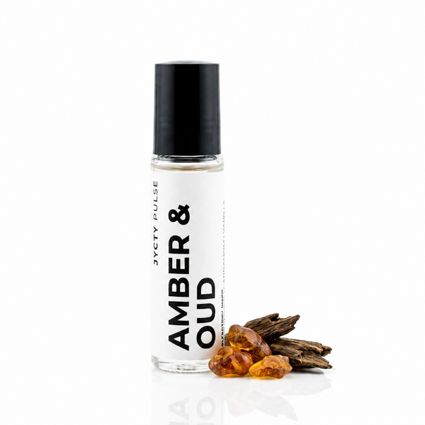 A clear glass roller bottle with a black cap and a white label reading 'AMBER & OUD' and 'JYCTY PULSE', shown on a white background with amber pieces and dried botanicals beside it.