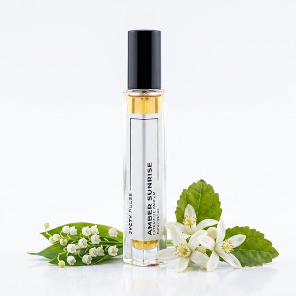 A clear cylindrical roller bottle with a black cap and amber liquid inside, labeled 'AMBER SUNRISE' BY JYCTY  styled with white flowers and green leaves on a clean white background.