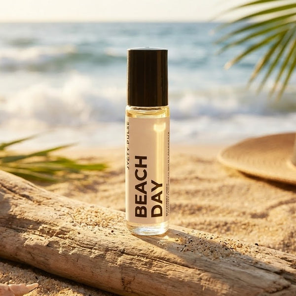 Roll-on bottle labeled 'Beach Day' on a sandy beach with ocean and palm leaves in the background.