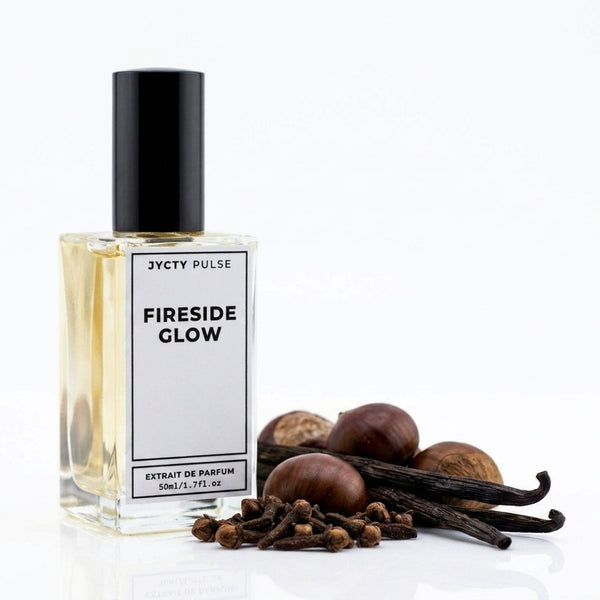 A clear rectangular perfume bottle with a black cap and a white label reading 'JYCTY PULSE' and 'FIRESIDE GLOW,' shown on a white background with vanilla beans, cloves, and chestnuts beside it.