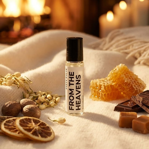 Rollerball perfume oil bottle labeled 'From the Heavens' surrounded by dried fruits, nuts, and chocolates on a soft fabric background.