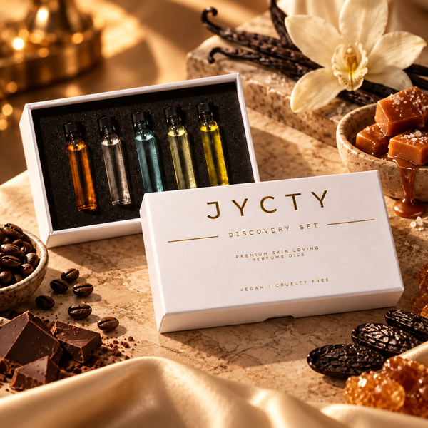 JYCTY Discovery Set premium skin-loving perfume oils in a white box, styled with vanilla orchid, chocolate, coffee beans, and caramel on a warm stone surface.