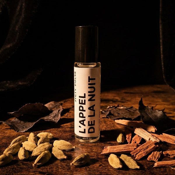 Perfume bottle labeled 'L'appel de la Nuit' on a wooden surface with dried herbs.