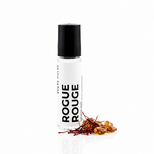 A clear glass roller bottle with a black cap and a white label reading 'ROGUE ROUGE' and 'JYCTY', shown on a white background with a small pile of amber-colored dried botanicals at the base.