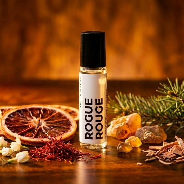 Roll-on bottle of 'Rogue Rouge' perfume oil on a wooden surface with dried fruits and flowers. Long lasting and vegan oil from JYCTY
