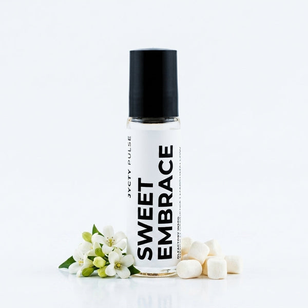 A clear 10ML bottle with a black cap and a white label reading 'SWEET EMBRACE' styled with small white blossoms and white candy cubes on a clean white background.