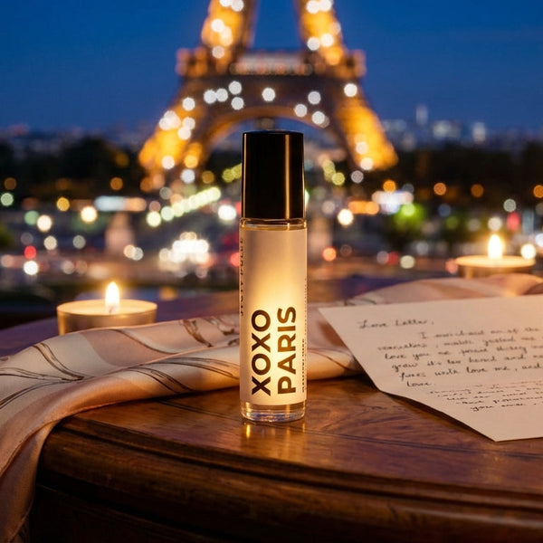 XOXO Paris perfume oil by JYCTY on a table with candles and a view of the Eiffel Tower at night.